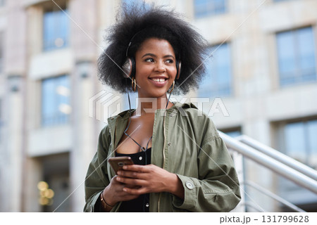 Music, phone and gen z black woman with headphones in city to relax and smile outside in street. Urban fashion, enjoying online streaming radio service and trendy girl listening to audio on earphones 131799628