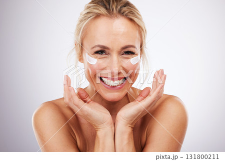 Skincare, eye cream and portrait of mature woman, anti ageing treatment and isolated on grey studio background. Health, skin and model face with smile and collagen mask on eyes in luxury spa facial. 131800211