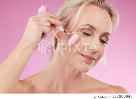 Face roller, beauty and woman facial massage with dermatology and cosmetic tools. Happy mature person on pink background for skincare, self care and rose quartz results for anti aging, glow and shine 131800946