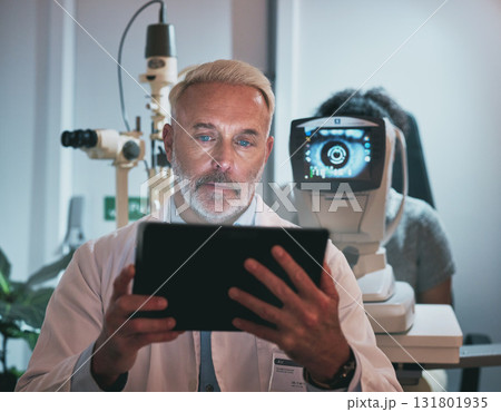 Digital tablet, optometry and man in a clinic doing optic research during eye care consultation. Ophthalmology, healthcare and senior male optometrist working on mobile device while doing vision test Digital tablet, optometry and man in a clinic doing optic research during eye care consultation. Ophthalmology, healthcare and senior male optometrist working on mobile device while doing vision test 131801935