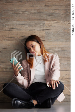 Young business woman, floor and texting with bored face on social media, app or phone in modern office. Professional female, smartphone and tired with search for email, chat or communication on break 131802237