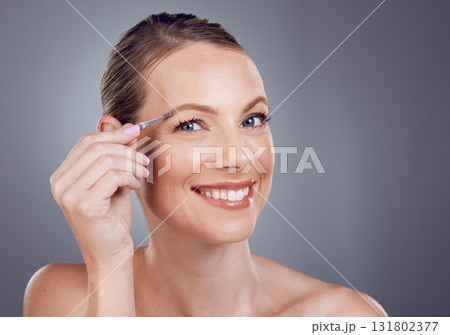 Eyebrows, grooming and portrait of a woman with a tweezers isolated on a grey studio background. Beauty, treatment and happy model plucking hair from face for shaping and routine on a backdrop 131802377