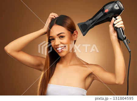 Woman, hair and hairdryer portrait in studio with smile for growth and color or healthy texture. Happy female hands with heat for haircare, self care and hairdresser or salon on brown background 131804595