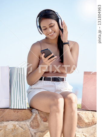 Woman relax after shopping, phone and headphones, listening to music outdoor with retail therapy and rest. Happy female, paper bag and communication with chat on social media app and technology Woman relax after shopping, phone and headphones, listening to music outdoor with retail therapy and rest. Happy female, paper bag and communication with chat on social media app and technology 131804963