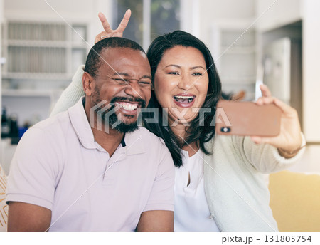 Senior black couple, selfie or happy in home together for silly, social media or relax with peace sign hand. Mature man, woman and digital photography app in house for embrace, bonding and bunny ears Senior black couple, selfie or happy in home together for silly, social media or relax with peace sign hand. Mature man, woman and digital photography app in house for embrace, bonding and bunny ears 131805754