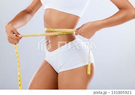 Weightloss, health and woman with measuring tape in a studio for her diet, exercise or wellness. Fitness, body and healthy slim female model checking the measurement of her waist by a gray background 131805921
