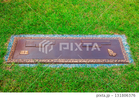 Bronze memorial plaque resting on lush green grass, honoring cherished individuals in peaceful cemetery Bronze memorial plaque resting on lush green grass, honoring cherished individuals in peaceful cemetery 131806376