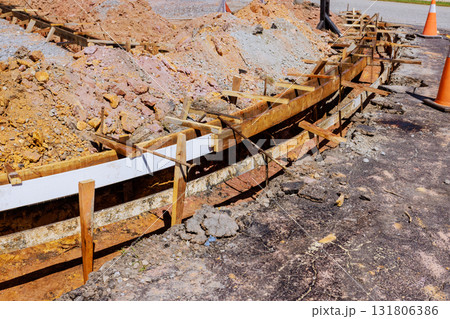 Workers prepare for curbed concrete installation at construction site with compacted soil wooden forms. 131806386
