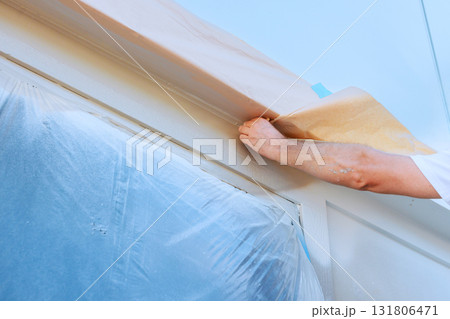 Worker carefully applying paper plastic sheets to protect areas before painting 131806471
