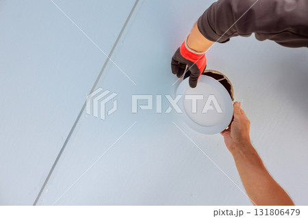 Electrician in gloves skillfully installs round ceiling light fixture in fresh, well lit room. Electrician in gloves skillfully installs round ceiling light fixture in fresh, well lit room. 131806479