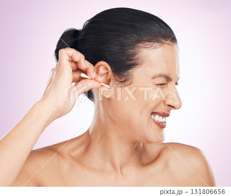 Woman, cotton bud and ear in studio for cleaning, struggle or pain for wellness by pink background. Model hand, self care or clean for hygiene, ears or natural product for healthy hearing by backdrop 131806656