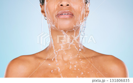 Face, water and shower with a black woman in studio on a blue background for hygiene or hydration. Splash, cleaning and bathroom with a young female washing her body for natural skincare or wellness 131806835