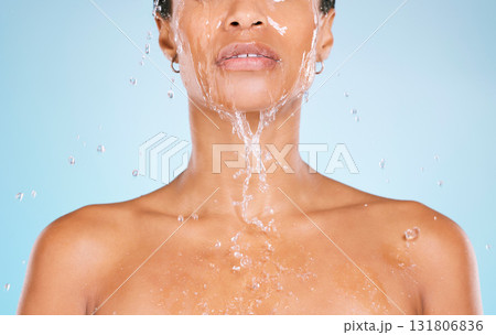 Face, water and cleaning with a black woman in studio on a blue background for hygiene or hydration. Splash, shower and bathroom with a young female washing her body for natural skincare or wellness 131806836
