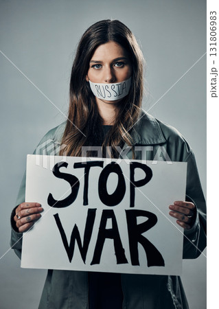 War, stop and portrait of a woman with a sign while silent isolated on a grey studio background. Protest, crime and silenced girl with a board against conflict and violence in Russia on a backdrop War, stop and portrait of a woman with a sign while silent isolated on a grey studio background. Protest, crime and silenced girl with a board against conflict and violence in Russia on a backdrop 131806983