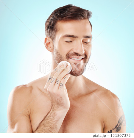 Skincare, cotton pad and man in a studio for health, grooming and hygiene facial routine. Beauty, wellness and handsome male model doing a fresh morning face treatment isolated by a blue background. 131807373