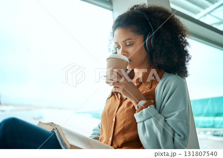 Airport, coffee and black woman reading a book by window waiting for global flight, departure and travel. International transport, lobby and girl with headphones for music, drinking beverage and read Airport, coffee and black woman reading a book by window waiting for global flight, departure and travel. International transport, lobby and girl with headphones for music, drinking beverage and read 131807540