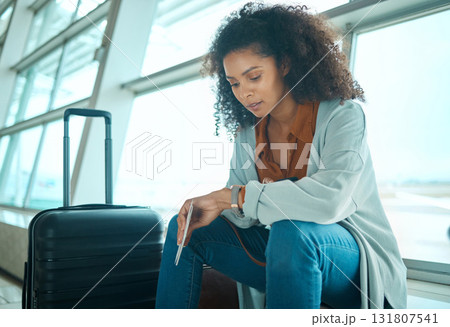 Airport, black woman and watch time check of a young female at plane terminal with flight delay. Waiting, sitting and person with passport document looking at smartwatch for board and transport info Airport, black woman and watch time check of a young female at plane terminal with flight delay. Waiting, sitting and person with passport document looking at smartwatch for board and transport info 131807541