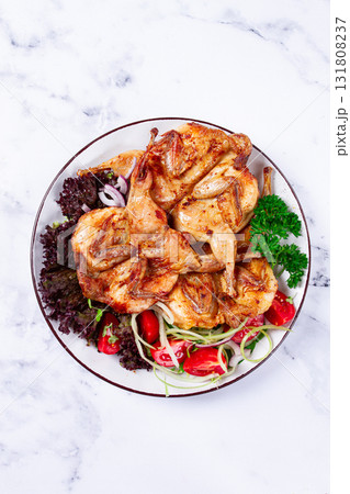 Baked quail, served on a plate with crispy lettuce leaves, fresh tomatoes and herbs, on a white plate, homemade, 131808237
