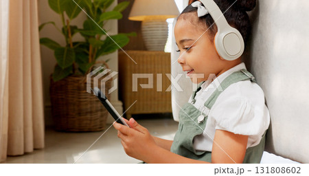 Tablet, headphones and girl child on the floor of her home, playing an online game to relax or for entertainment. Technology, music and smile with a happy young kid distance learning on the internet 131808602