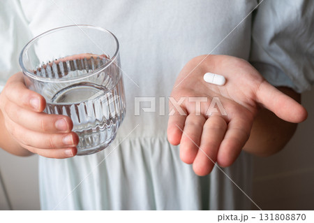 Pill and glass with water in the hand of child. Healthcare from pharmacy. Kid sit at home because of illness. Pill and glass with water in the hand of child. Healthcare from pharmacy. Kid sit at home because of illness. 131808870