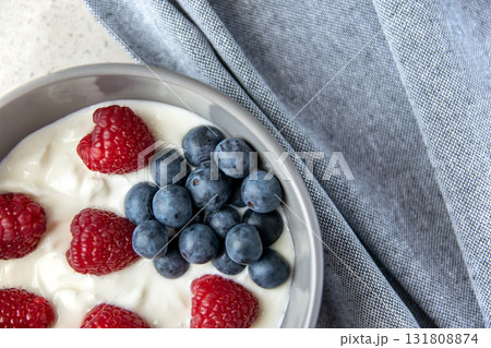 Natural fresh greek yogurt with red and blue berries in the grey plate and napkin for healthy breakfast. Black stone background. Natural fresh greek yogurt with red and blue berries in the grey plate and napkin for healthy breakfast. Black stone background. 131808874