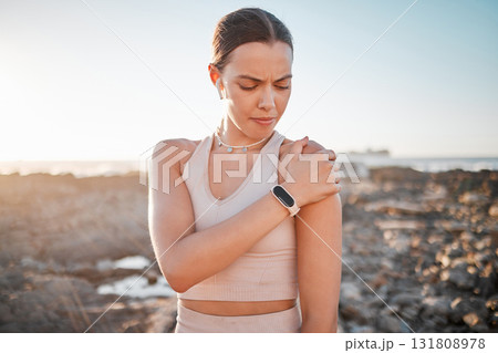 Beach, fitness and yoga, woman with shoulder pain standing on rocks at ocean. Nature, sports and injury during workout for health and wellness, muscle trauma during stretching exercise in morning. Beach, fitness and yoga, woman with shoulder pain standing on rocks at ocean. Nature, sports and injury during workout for health and wellness, muscle trauma during stretching exercise in morning. 131808978