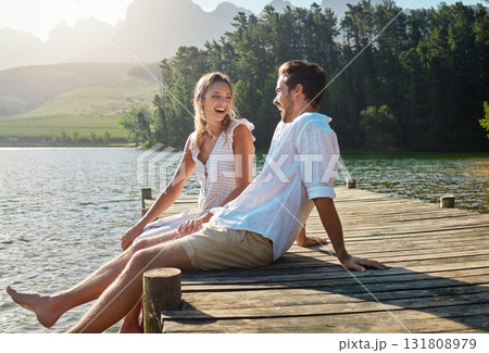 Love, laugh and pier with couple at lake for bonding, romance and affectionate date. Nature, travel and holiday with man and woman sitting on boardwalk in countryside for happy, summer and vacation 131808979