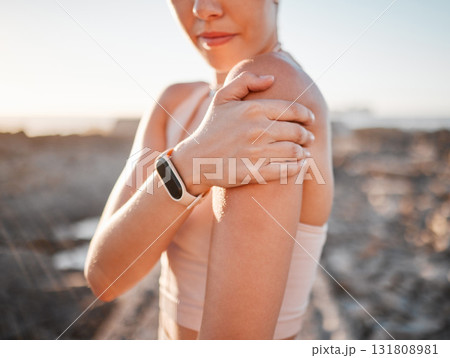Beach, fitness and woman with hand on shoulder pain standing on rocks at ocean. Nature, sports and injury during workout for health and wellness, muscle trauma during stretching exercise in morning. 131808981