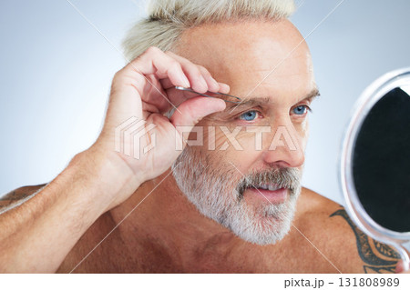 Senior man, bathroom tweezers and mirror check in a studio doing hair removal and grooming. Wellness, eyebrows and beauty routine of a male model care with grey background and steel tools for face Senior man, bathroom tweezers and mirror check in a studio doing hair removal and grooming. Wellness, eyebrows and beauty routine of a male model care with grey background and steel tools for face 131808989