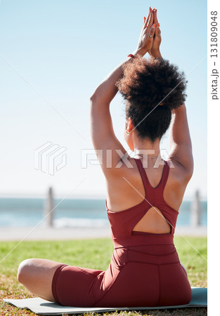Fitness, black woman and meditation on yoga mat by beach for spiritual wellness or exercise in nature. Sporty female yogi back in warm up arm stretch for zen workout, relax or awareness in meditating 131809048