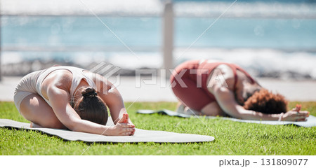 Woman, yoga friends and stretching on grass for wellness, strong legs and body in morning sunshine by sea. Women teamwork, fitness and workout by ocean with support, focus and mindfulness in summer 131809077