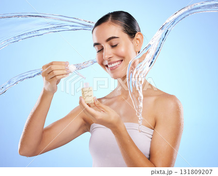 Happy woman, dropper and water splash for skincare serum, product or hygiene against blue studio background. Calm female smile holding pipette for beauty cosmetics, essential oil or facial treatment 131809207