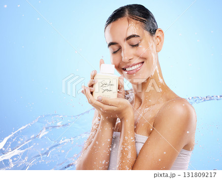 Happy woman, water splash and face with skincare serum, product or cream against blue studio background. Calm female smile holding moisturizer creme for beauty cosmetics or facial treatment on mockup 131809217