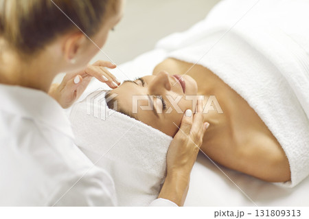 Beautiful woman with closed eyes relaxes in spa center during facial massage. 131809313