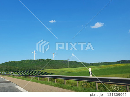 Three white windmills with green field and blue sky. Wind turbine and solar panels (solar cell) in solar farm for alternative green energy in Europe. Three white windmills with green field and blue sky. Wind turbine and solar panels (solar cell) in solar farm for alternative green energy in Europe. 131809963