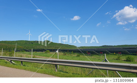 Three white windmills with green field and blue sky. Wind turbine and solar panels (solar cell) in solar farm for alternative green energy in Europe.  131809964