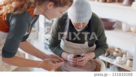 Pottery, teacher and woman learning in workshop, studio and artist training process with a craft wheel and creativity in clay sculpture. Helping, hands and teaching student in creative potter class 131810108