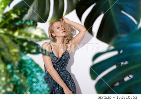 Fashion portrait of a model in a green dress surrounded by tropical leaves, vibrant lighting and editorial styling creating resortwear and beauty concept imagery 131810552
