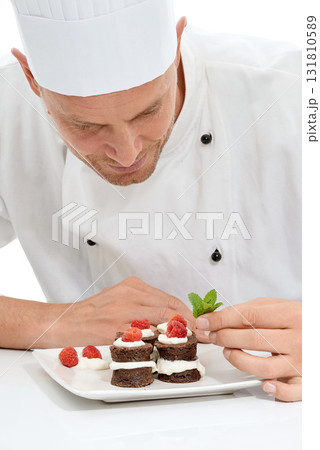 Chef, dessert and mint on sweet food by culinary cook with chocolate recipe on a plate isolated in white studio background. Cooking, presentation and man making mini cakes as cuisine for fine dining 131810589