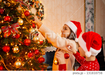 Teenage girl decorating Christmas tree, her younger brother helps her, holding baubles. Cheerful children decorating Christmas tree at home Teenage girl decorating Christmas tree, her younger brother helps her, holding baubles. Cheerful children decorating Christmas tree at home 131810738
