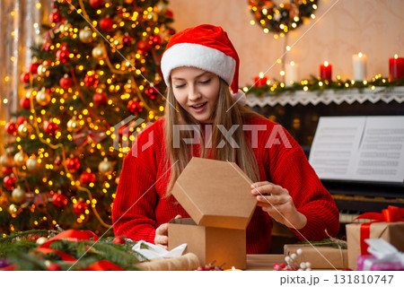 Young girl opens Christmas present. Surprised blonde girl in decorated living room opens box gift from friend for Christmas Young girl opens Christmas present. Surprised blonde girl in decorated living room opens box gift from friend for Christmas 131810747