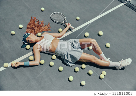 Fashion, tennis and woman lying on the court with a racket and balls after a game or practice. Fitness, sports and portrait of a female athlete relaxing at the outdoor stadium after match or training Fashion, tennis and woman lying on the court with a racket and balls after a game or practice. Fitness, sports and portrait of a female athlete relaxing at the outdoor stadium after match or training 131811003