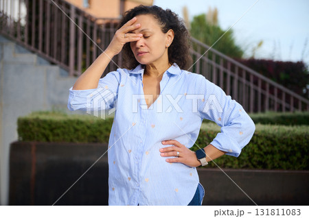 Confident Woman In Blue Striped Shirt Outdoors, Hands On Forehead In Moment Of Stress 131811083