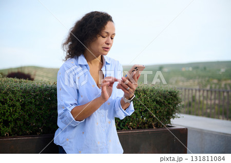 Woman Using Smartphone Outdoors By Hedge, Checking Messages On Phone During Daytime Woman Using Smartphone Outdoors By Hedge, Checking Messages On Phone During Daytime 131811084
