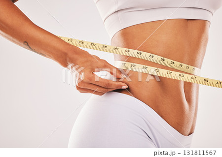 Weight, fat and woman with tape for stomach isolated on a grey studio background. Insecurity, health and girl measuring her body for slim shape, cellulite and belly while standing on a backdrop Weight, fat and woman with tape for stomach isolated on a grey studio background. Insecurity, health and girl measuring her body for slim shape, cellulite and belly while standing on a backdrop 131811567