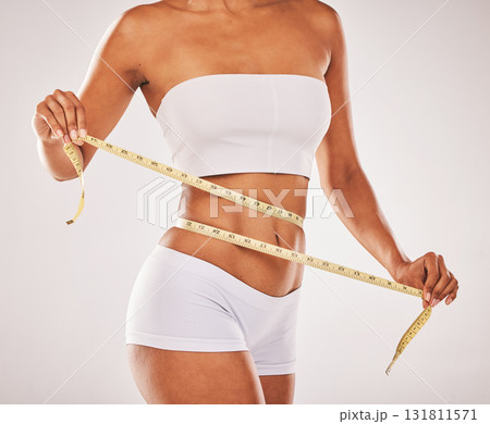 Lose weight, body and woman with tape for stomach isolated on a grey studio background. Diet, health and girl measuring her waist for slim shape, motivation and belly while standing on a backdrop Lose weight, body and woman with tape for stomach isolated on a grey studio background. Diet, health and girl measuring her waist for slim shape, motivation and belly while standing on a backdrop 131811571