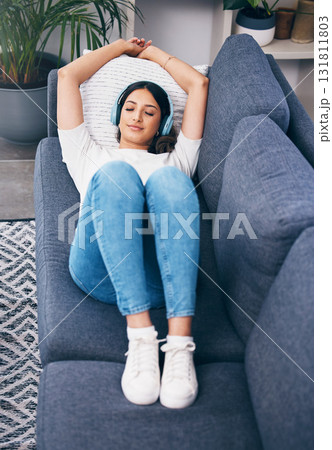 Music, relax and lying with a woman in her home, listening to the radio while on a sofa in the living room. Peace, wellness or headphones with an attractive young female streaming audio in a house 131811803