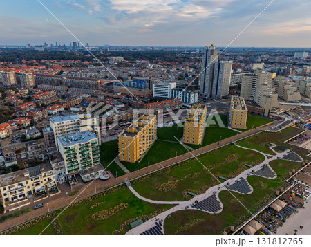Hague, South Holland, Netherlands - 09.06.2025: Aerial view of coastal city with angular golden brown buildings on green lawn, beach promenade, and dense urban sprawl blending modern 131812765