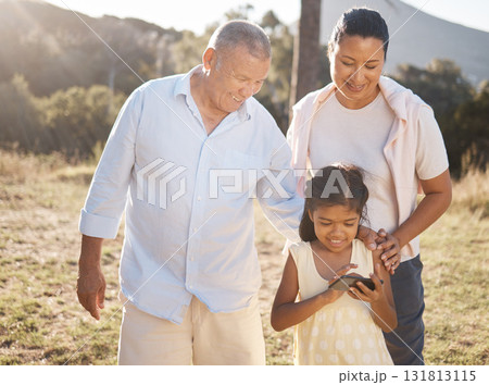 Phone, family and nature with a girl and grandparents outdoor together during summer vacation. Social media, love and care with a senior man and woman bonding with their female grandchild outside Phone, family and nature with a girl and grandparents outdoor together during summer vacation. Social media, love and care with a senior man and woman bonding with their female grandchild outside 131813115
