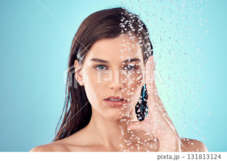 Face, water splash and skincare of woman in shower in studio isolated on a blue background. Beauty, portrait and young female model washing, cleaning or bathing for hygiene, wellness and health. 131813124